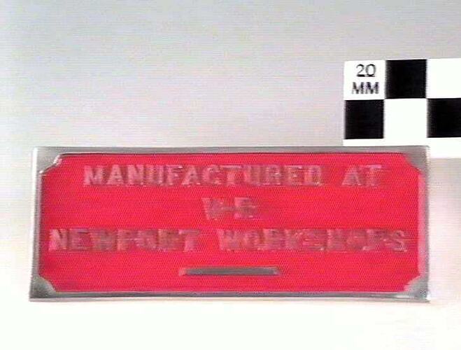 Rectangular red metal plate with raised lettering.