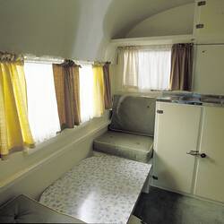 Caravan internal view of green seats, low table and cream cupboards.