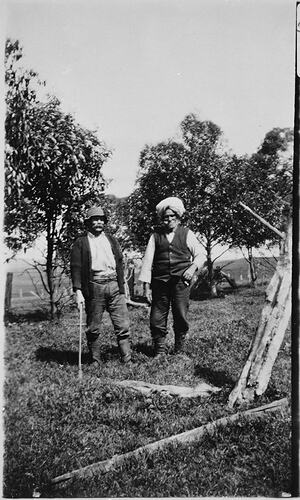 Two men standing outdoors on a farm. The man on the right wears a turban.