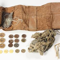 Sewing kit with contents displayed beside. Numerous buttons, rusted needles and thread.