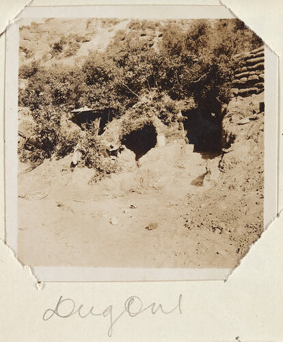 Sloping dirt and scrub covered landscape with the entranceway to a shelter in the mid ground.