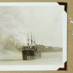 Boat in water with smoke billowing, land and trees in background.