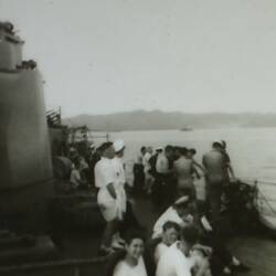 Sailors on the deck of a ship in foreground, land in the background.
