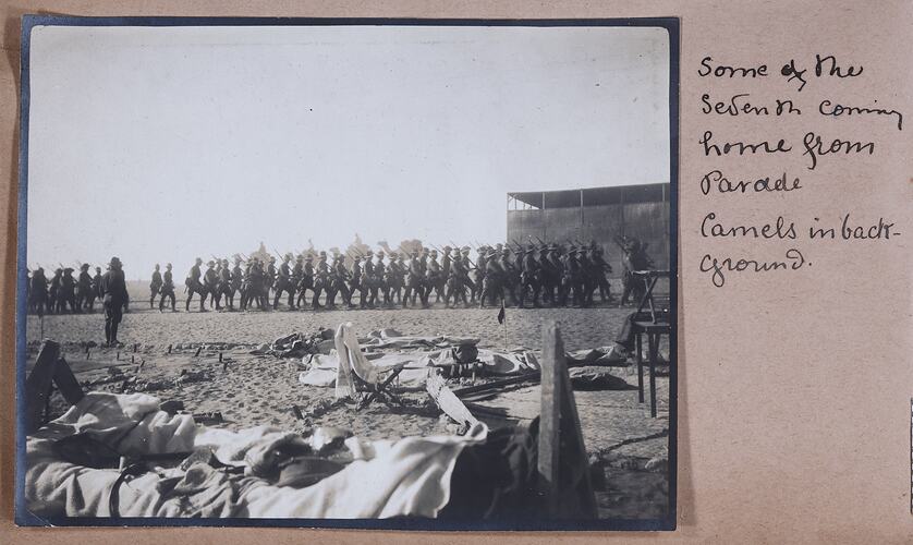 Photo of soldiers marching in formation, makeshift beds in foreground, handwritten text on right of photo.