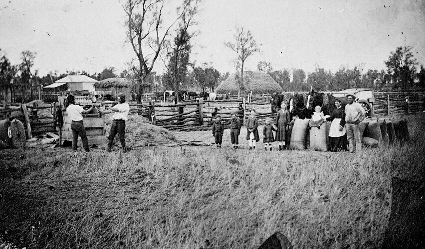 Family group in farmyard posing in front of row of full wheat sacks.