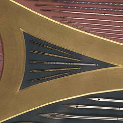 Detail of panel made of needles, crochet hooks, surgical needles, and other needles and needle cases. In red, black and yellow.
