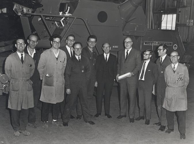 A group of men standing in front of a harvester.