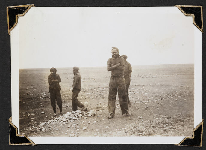Four men standing with flat clear landscape behind.