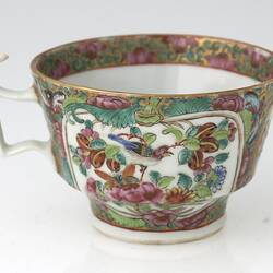 Decorative teacup with colourful Chinese scene that includes a bird and flowers.