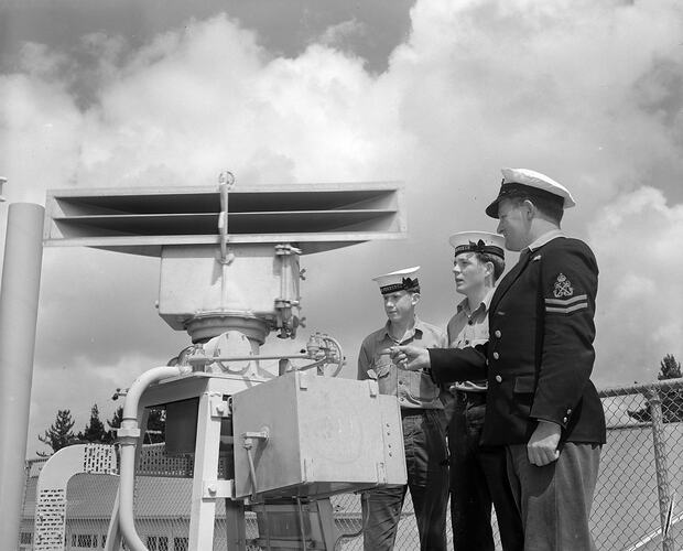 Three men in sailor uniforms standing next to naval equipment.