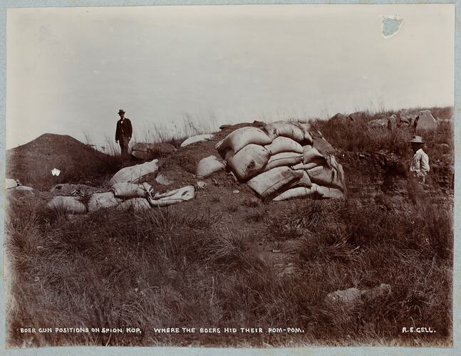 Two men standing on hill with near piles of sand bags.