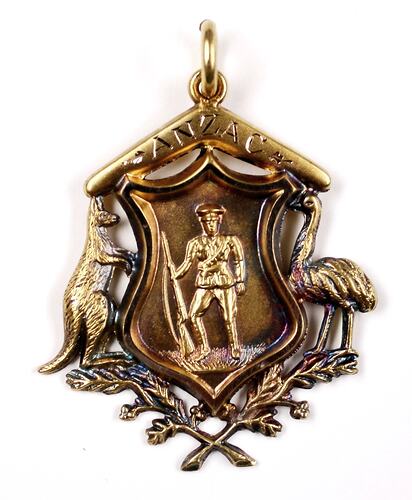 Gold ornament of Australian coat of arms with soldier holding rifle at centre, inscribed boomerang on top.