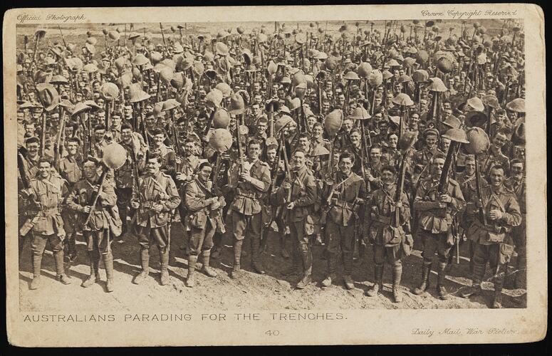 Many Australian soldiers smile as they hold their helmets up above their heads on their rifles.
