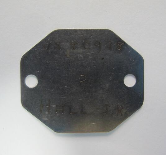 Metal tag, hexagonal, with hole at each side and engraved text.