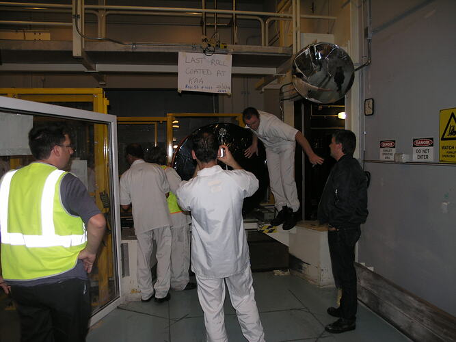 People in factory with handmade sign above.