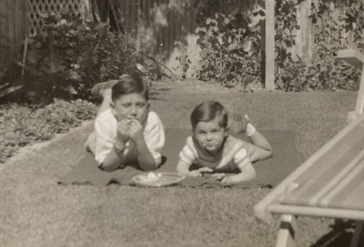 Two children lying in suburban backyard.