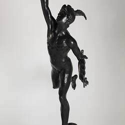 Metal statue of figure standing on an orb carrying a lamp and caduceus. Left view.