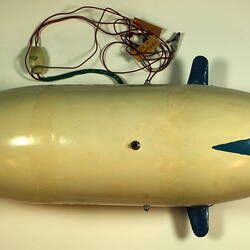 White model airship with blue nose and wings. Cables above. Top view.