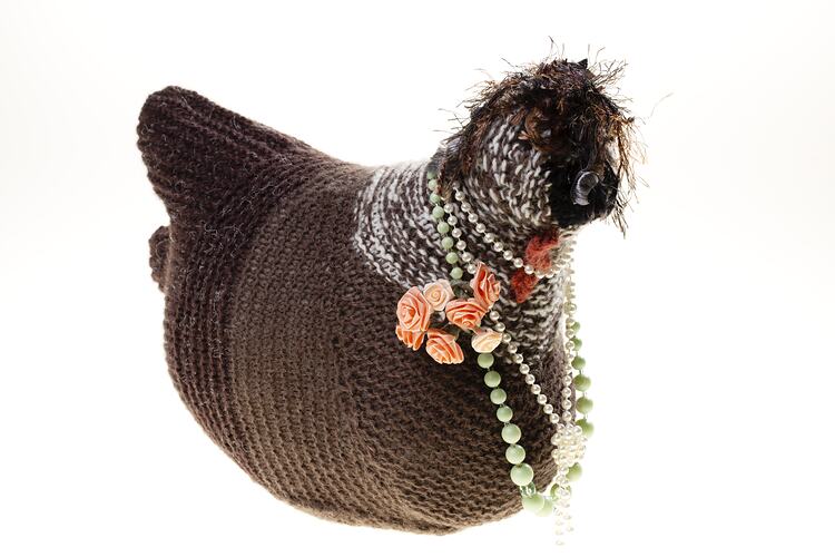 Hand-knitted brown chicken with pink rosettes and necklaces around its neck.