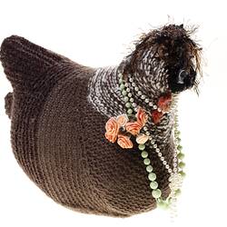 Hand-knitted brown chicken with pink rosettes and necklaces around its neck.