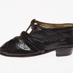 Miniature hand-sewn black leather shoe with strap and glass button fastener. Left profile.