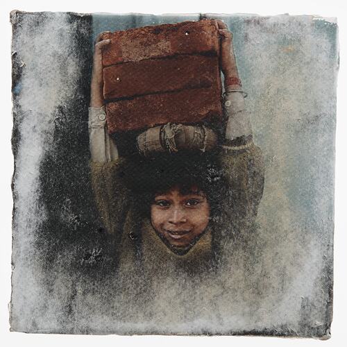 Portrait of boy carrying bricks on his head.