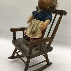 Hedgehog doll standing in wooden rocking chair.