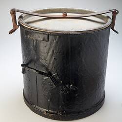 Black metal bucket with lid and one handle on side. Metal clip holds down lid.