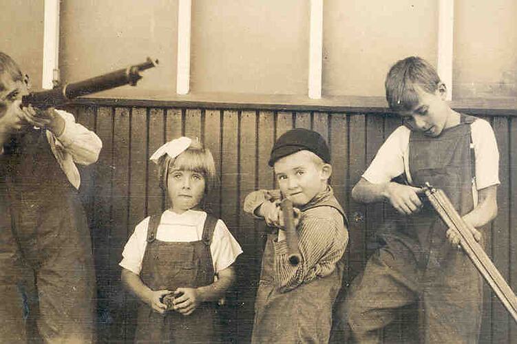 Four year old girl with her three older brothers who all hold rifles.