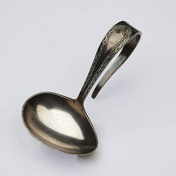 Silver spoon with u-shaped decorative handle. Bowl of the spoon is oval, tapered at one end. Tilted view.