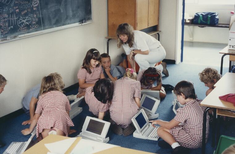 A group of students sitting on the floor working with laptops.