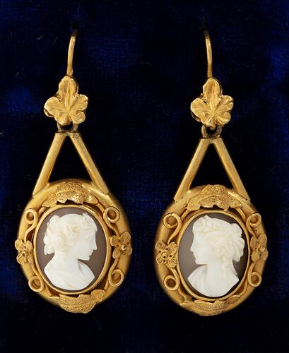 Pair of decorative gold mounted cameo earrings. The matched cameos are of a classical woman's profile with cloth draped over the shoulder and with a ringlet of hair falling behind an ear. One profile faces right, the other, left.