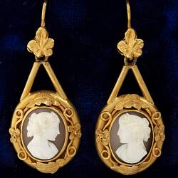 Pair of decorative gold mounted cameo earrings. The matched cameos are of a classical woman's profile with cloth draped over the shoulder and with a ringlet of hair falling behind an ear. One profile faces right, the other, left.