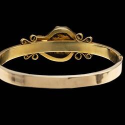 Back of gold bangle (bracelet) featuring a large gold nugget. Fine chain hanging at left.