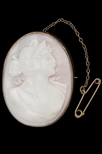 Oval white brooch with cameo of female bust in gold setting with safety chain.