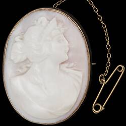 Oval white brooch with cameo of female bust in gold setting with safety chain.