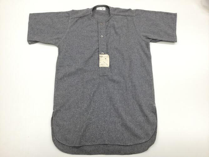 Grey flannel shirt with label adhered to front. Short sleeved, three buttons at neck.