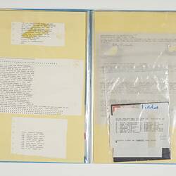 Open blue folder. White pages on left and right have printed text. Floppy disk on right.