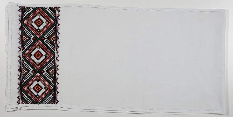 White cotton cloth with embroidered geometric pattern band along left edge.