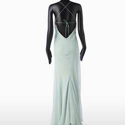 Back view of full length pale green silk evening slip dress. Sleeveless. Fastens at back with long green silk covered rope ties. Flared/fishtail skirt.
