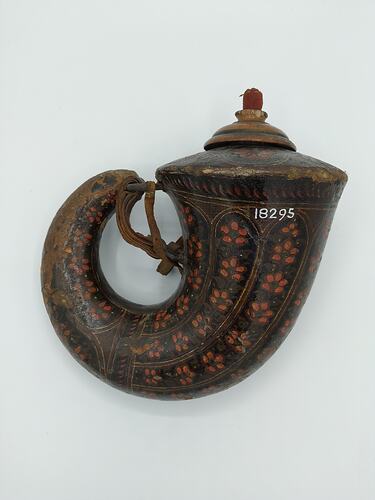 Volute shaped wood flask covered with red patterned papier mache. Wide sealed opening with wooden stopper curls to thin spout. Has strap.