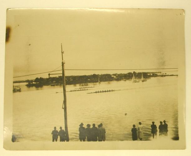 Row of men and women watching boat race.