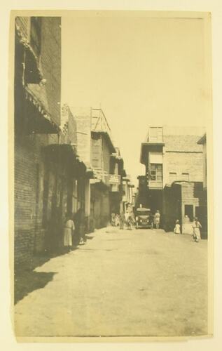 Narrow street with buildings either side, people and cars.
