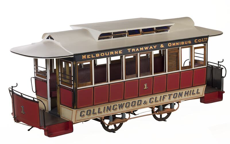 Red and white cable tram model with nine windows on each side, four wheels and painted lettering.