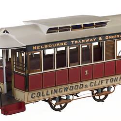 Red and white cable tram model with nine windows on each side, four wheels and painted lettering.