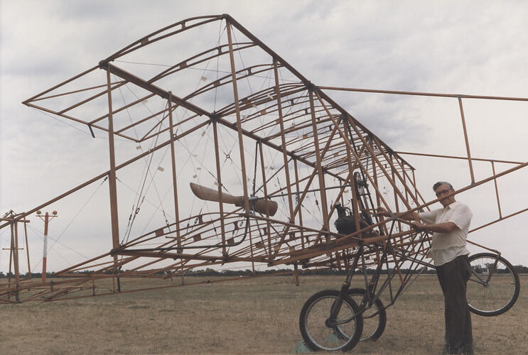 Man with airframe of biplane in field.