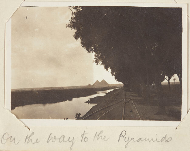 River with tree lined railway track, pyramids in the background.