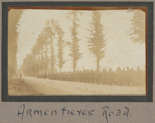 Servicemen marching in a line down a tree lined dirt road.