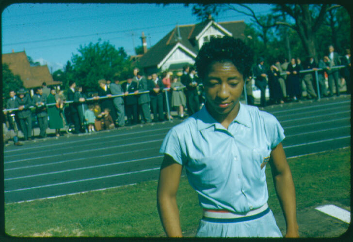 American female athlete standing alongside a running track.