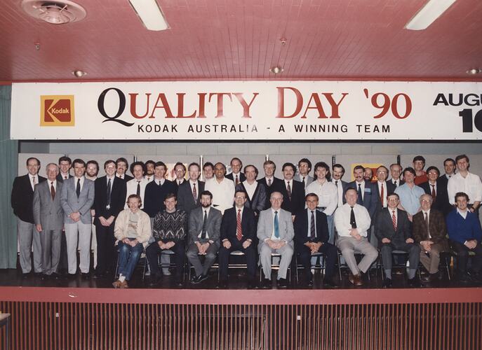 Large group on stage under Quality Day sign.